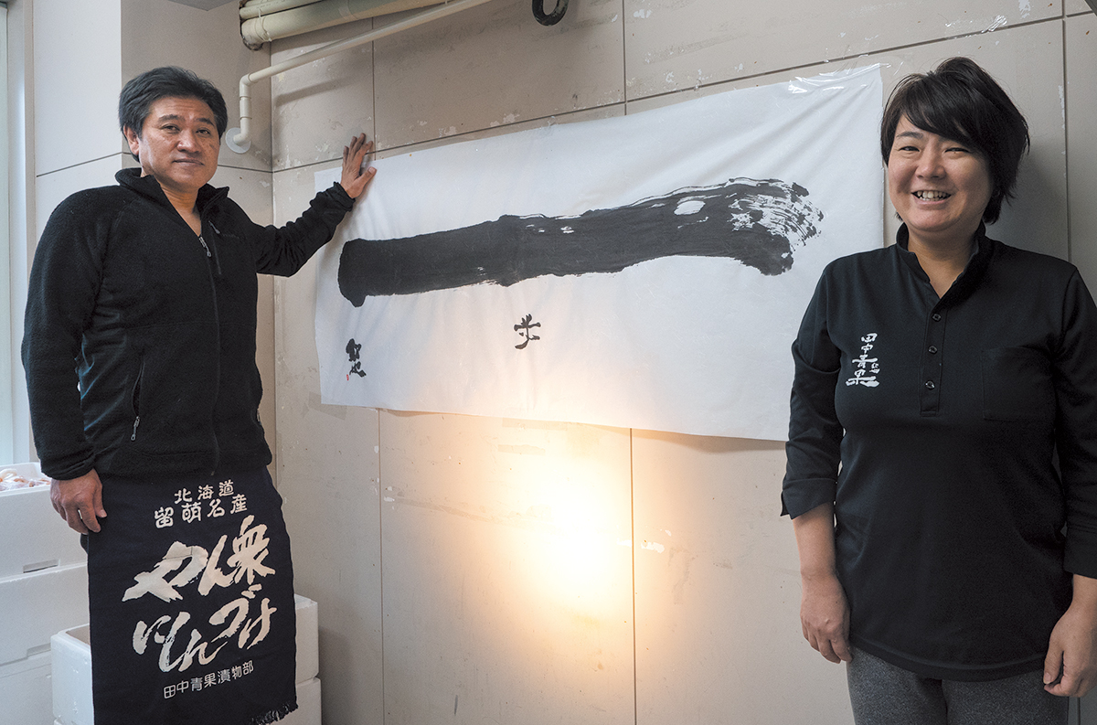 自ら書いた「一」の字の前の田中欽也さんと、美智子さん。