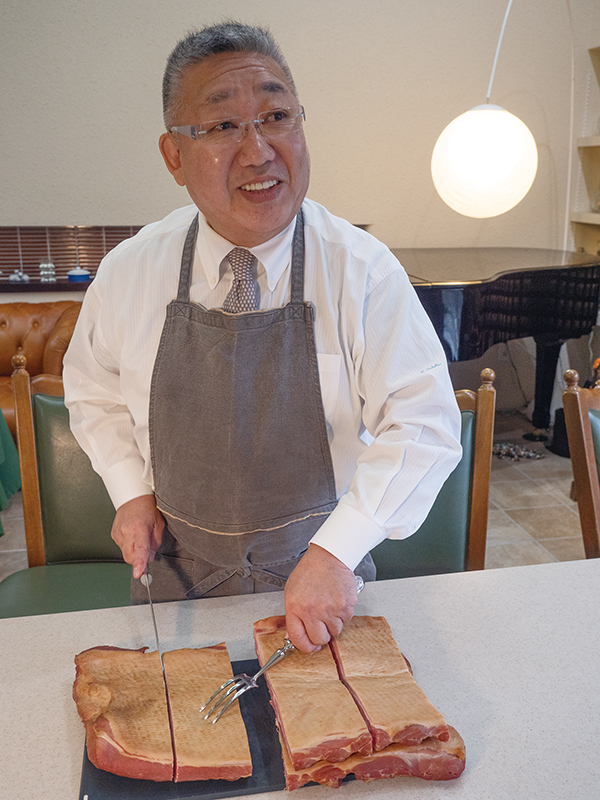 店主の田畑広司さん。道外の物産展での販売も多い。お客さんに接するときは、ワイシャツにネクタイでベーコンを切り分ける。