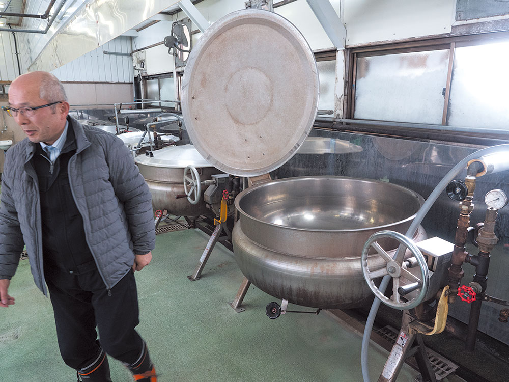社長の谷全悦夫さんに工場内を案内してもらう。豆を煮る大きな釜が並ぶ。